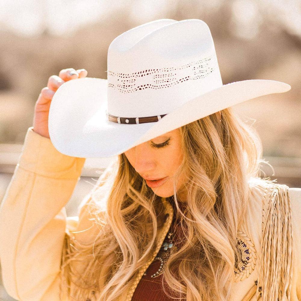 Woman wearing a white cowboy hat with a blurred natural background